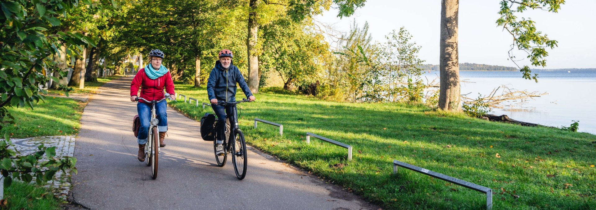 Twee fietsers op een met bomen omzoomd pad aan de oever van het meer van Schwerin, omringd door herfstachtige natuur.