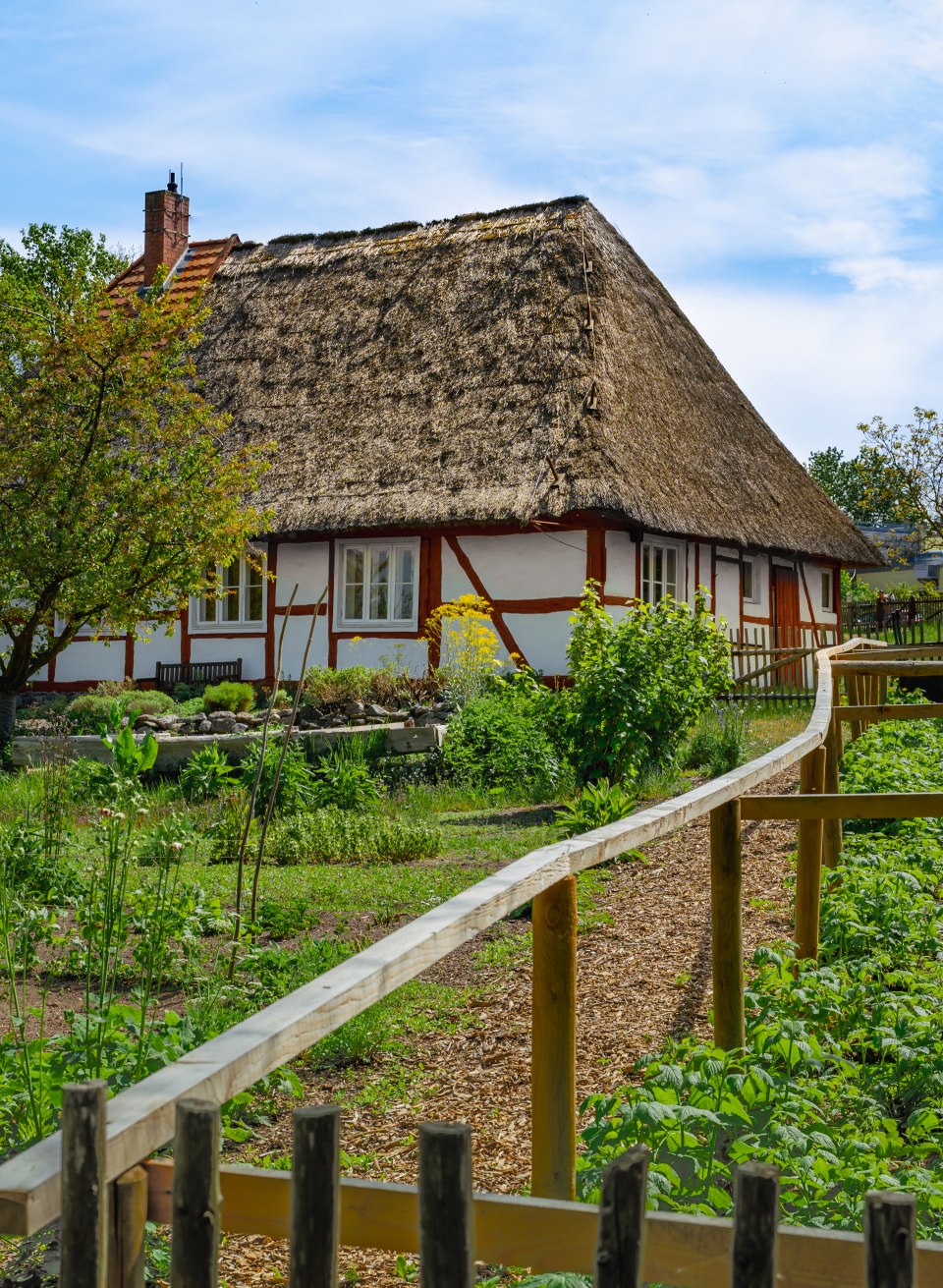 De tuin van de dorpsonderwijzer in het openluchtmuseum Mueß met een vakwerkhuisje met rieten dak.