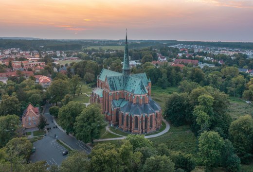Widok z lotu ptaka na katedrę w Bad Doberan o zachodzie słońca, otoczoną drzewami, łąkami i okolicznym miastem.