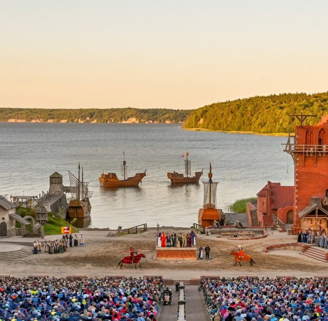 Podium van het Störtebeker Festival in Ralswiek op Rügen met publiek, middeleeuws decor en uitzicht op de Oostzee.