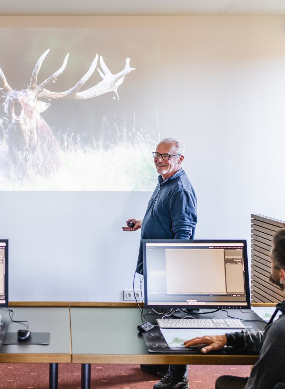 Een docent presenteert een foto van een hert aan workshopdeelnemers in het Max H&uuml;nten Haus.