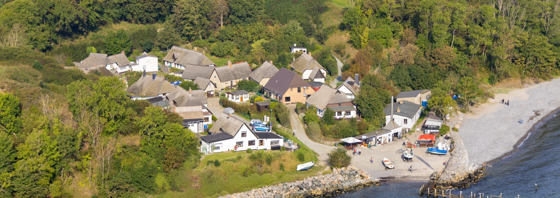 Luchtfoto van het vissersdorp Vitt op het eiland Rügen. Je ziet huizen met rieten daken, groene weiden op de achtergrond en de Oostzeekust met een klein havengebied op de voorgrond.