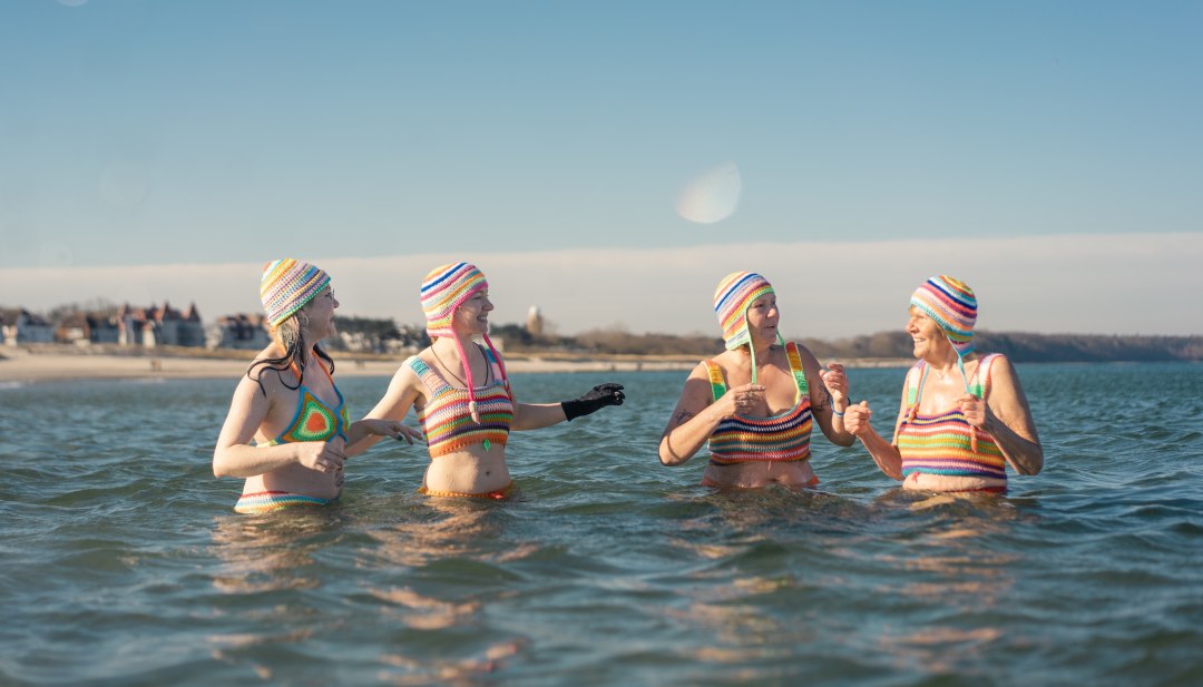 Kleurrijke winterpret - vier vrouwen genieten van het ijskoude water van de Baltische Zee in kleurrijke gebreide bikini's tijdens een verfrissende duik voor de kust van Mecklenburg-Vorpommern., © TMV/Gross Vier vrouwen in kleurrijke gebreide bikini's genieten van een winterse duik in de Baltische Zee voor de kust van Mecklenburg-Vorpommern.