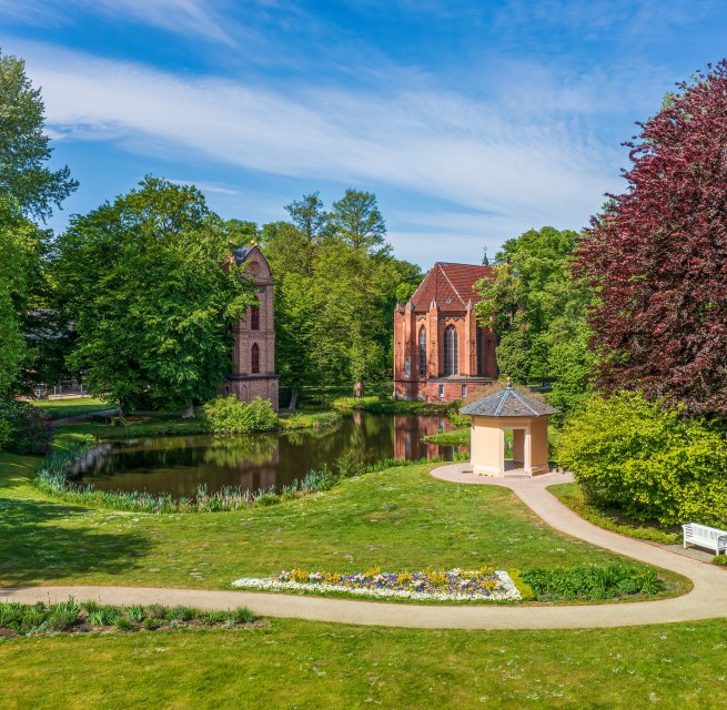 Bell tower and park building in Ludwigslust Palace Gardens with flowers and trees.
