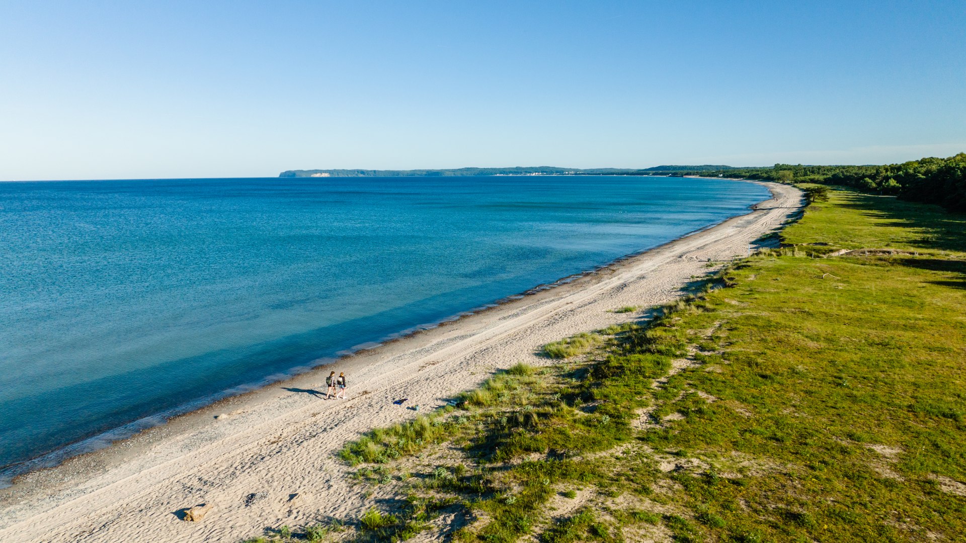 Two women walking on the natural beach at Mukran. View from the air with the Baltic Sea in the background.