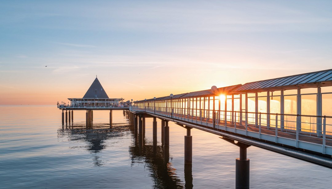 De pier van Heringsdorf op Usedom in het gouden licht van de zonsopgang boven de kalme Baltische Zee. // Magische zonsopgang over de Baltische Zee - de pier van Heringsdorf op Usedom betovert met zijn architectonische elegantie en een van de mooiste panoramische uitzichten van het eiland. // © Kaiserbaeder Tourismus Service GmbH De pier van Heringsdorf op Usedom in het gouden licht van de zonsopgang boven de kalme Baltische Zee.