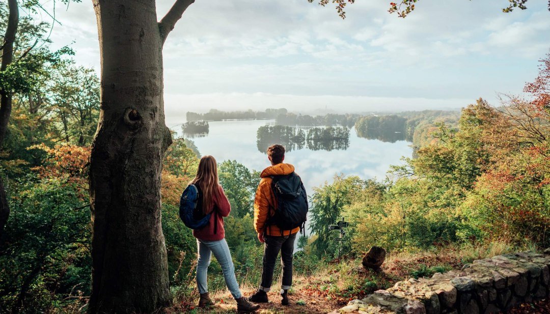 A couple looks down from the Reiherberg in Feldberg onto the Feldberger Haussee // Hiking on the nature park trail at the Reiherberg viewpoint in Feldberg // © MV-T/Gänsicke A couple looks down from the Reiherberg in Feldberg onto the Feldberger Haussee