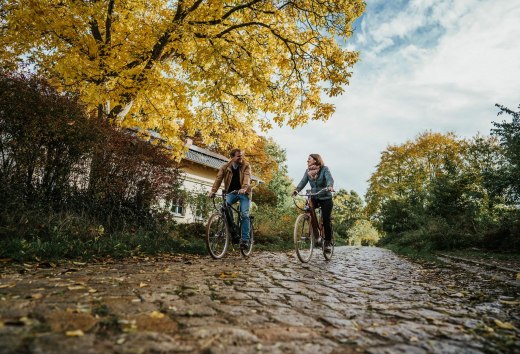 Op stap met de fiets op het landgoed Pohnstorf in de herfst, © 1000seen Twee mensen fietsen op kasseien in de buurt van het landgoed Pohnstorf in de herfst.
