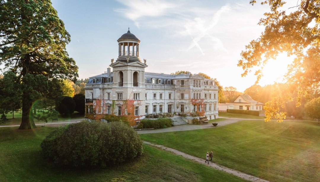 Kaarz Castle in Mecklenburg-Schwerin at sunset with walkers in the well-tended castle park. // Evening atmosphere in Mecklenburg-Schwerin - Kaarz Castle shines in the warm light of the setting sun and invites you to take a relaxing stroll through the historic parkland. // © MV-T/Gross Kaarz Castle in Mecklenburg-Schwerin at sunset with walkers in the well-tended castle park.