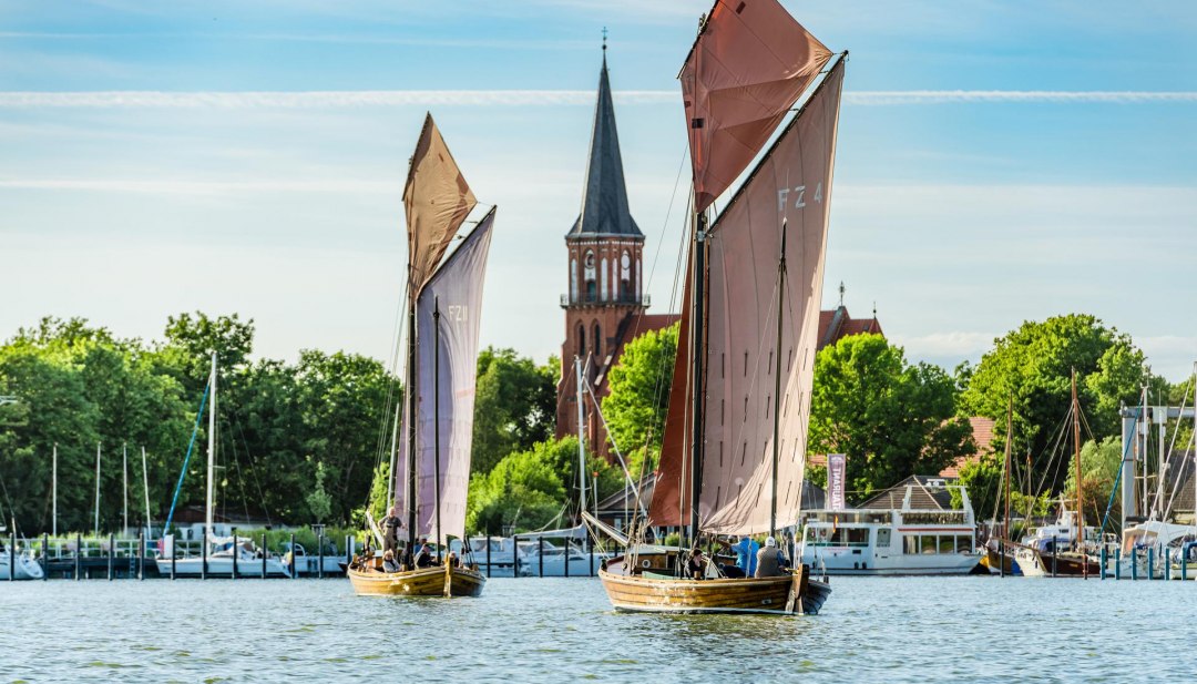 Twee Zeesen boten varen op de Bodden voor de haven van Wustrow met uitzicht op de dorpskerk. // © MV-T/Tiemann Twee Zeesen boten varen op de Bodden voor de haven van Wustrow met uitzicht op de dorpskerk.
