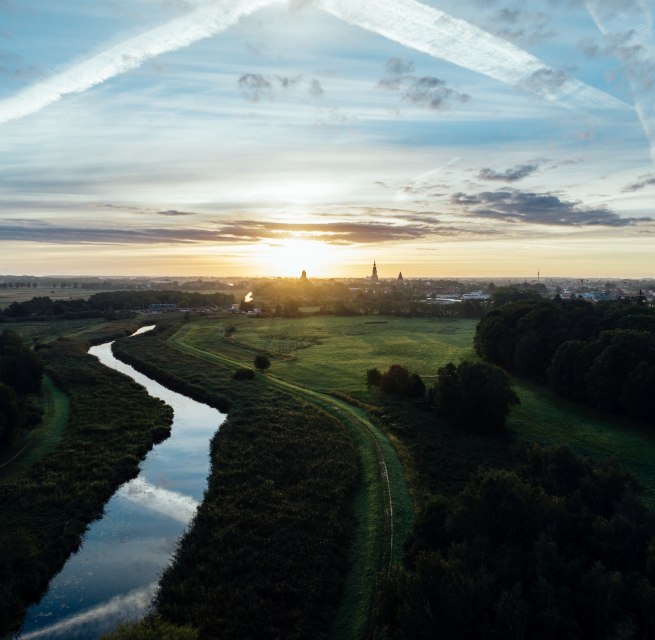 Sonnenaufgang &uuml;ber der Hansestadt Greifswald: Ein stiller Fluss schl&auml;ngelt sich durch Wiesen, w&auml;hrend Kircht&uuml;rme am Horizont langsam im Morgenlicht sichtbar werden. Mecklenburg-Vorpommern erwacht leise. // &copy; MV-T/G&auml;nsicke