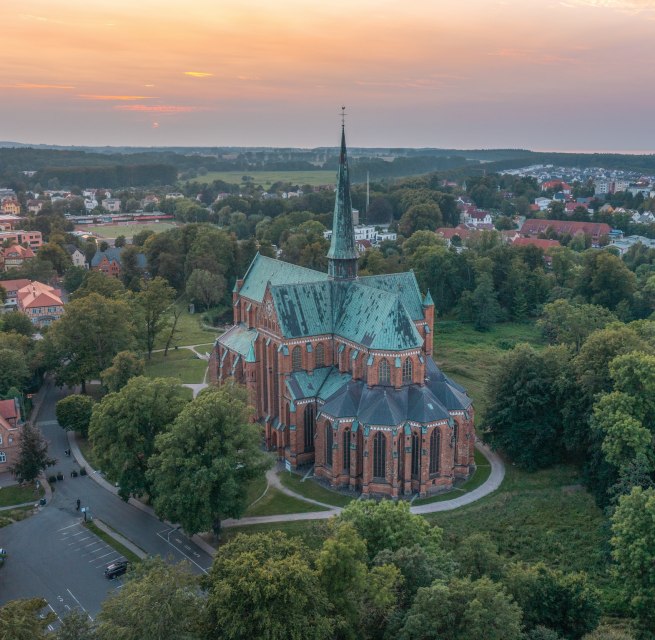 Aerial view of the cathedral in Bad Doberan at sunset, surrounded by trees, meadows and the surrounding town.
