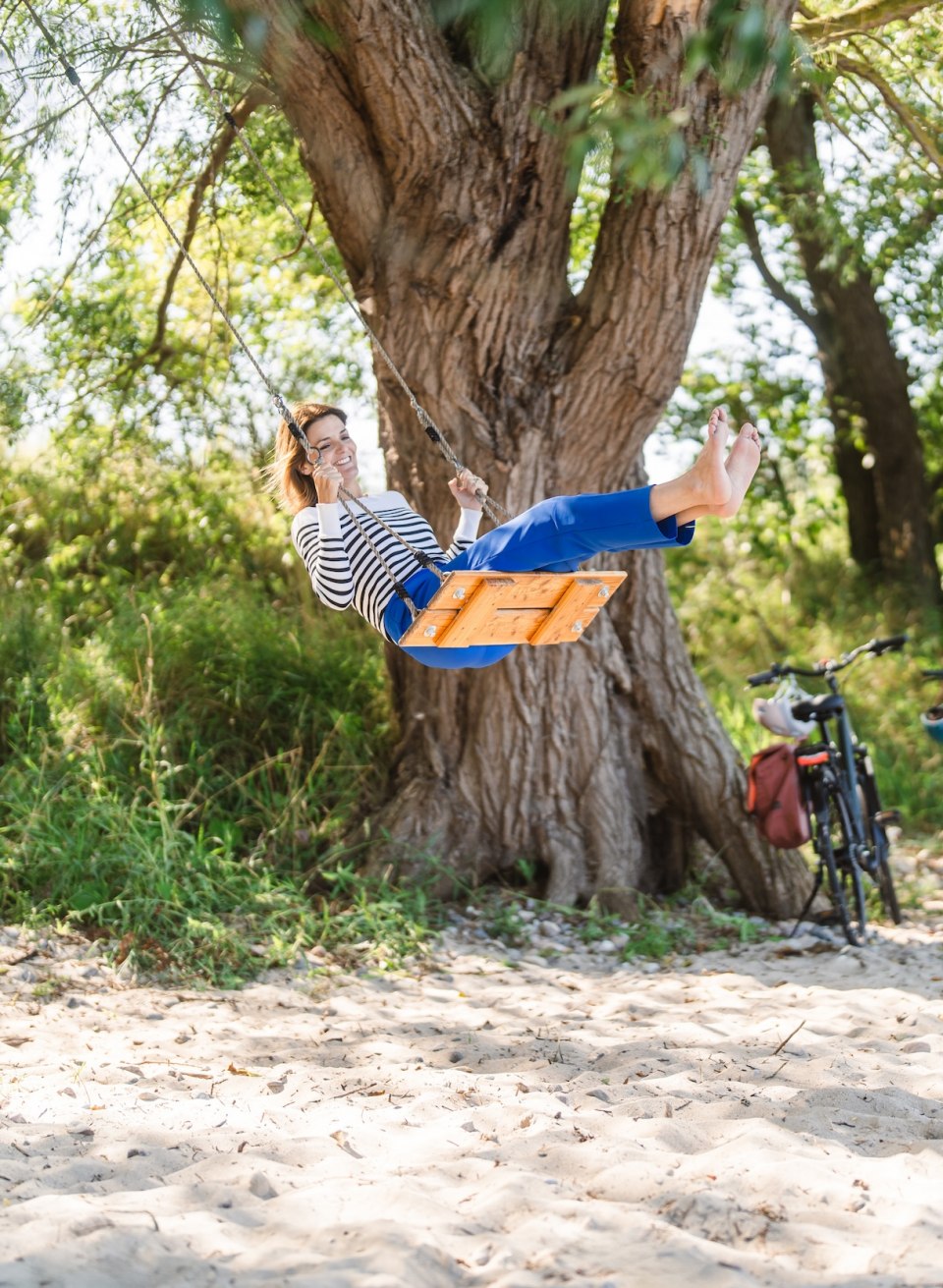 The North German Romantic Route also has some unexpected highlights in store., © TMV/Gross A woman swings on the beach under a tree near Lubmin.