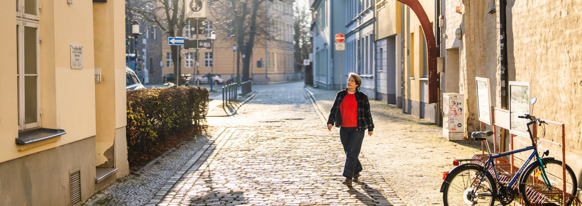 Kobieta spacerująca brukowaną uliczką w centrum starego miasta Greifswald w promieniach słońca.
