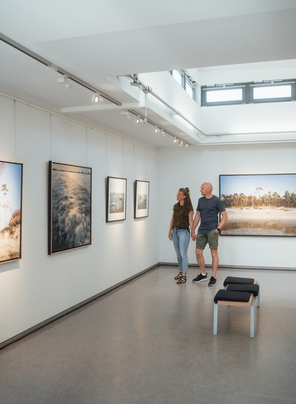 Hand in hand, picture by picture: You can admire art and take creative courses in Ahrenshoop's numerous galleries., © TMV/Petermann A couple strolls through a gallery. Nature photographs hang on the walls.