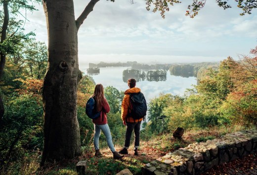 A couple looks down from the Reiherberg in Feldberg onto the Feldberger Haussee // Hiking on the nature park trail at the Reiherberg viewpoint in Feldberg // © MV-T/Gänsicke A couple looks down from the Reiherberg in Feldberg onto the Feldberger Haussee