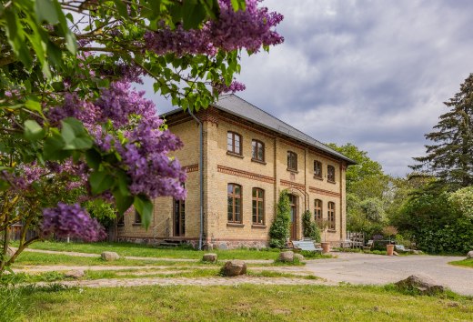 Dworek w Lexow z kwitnącymi bzami na pierwszym planie i zabytkową ceglaną fasadą.