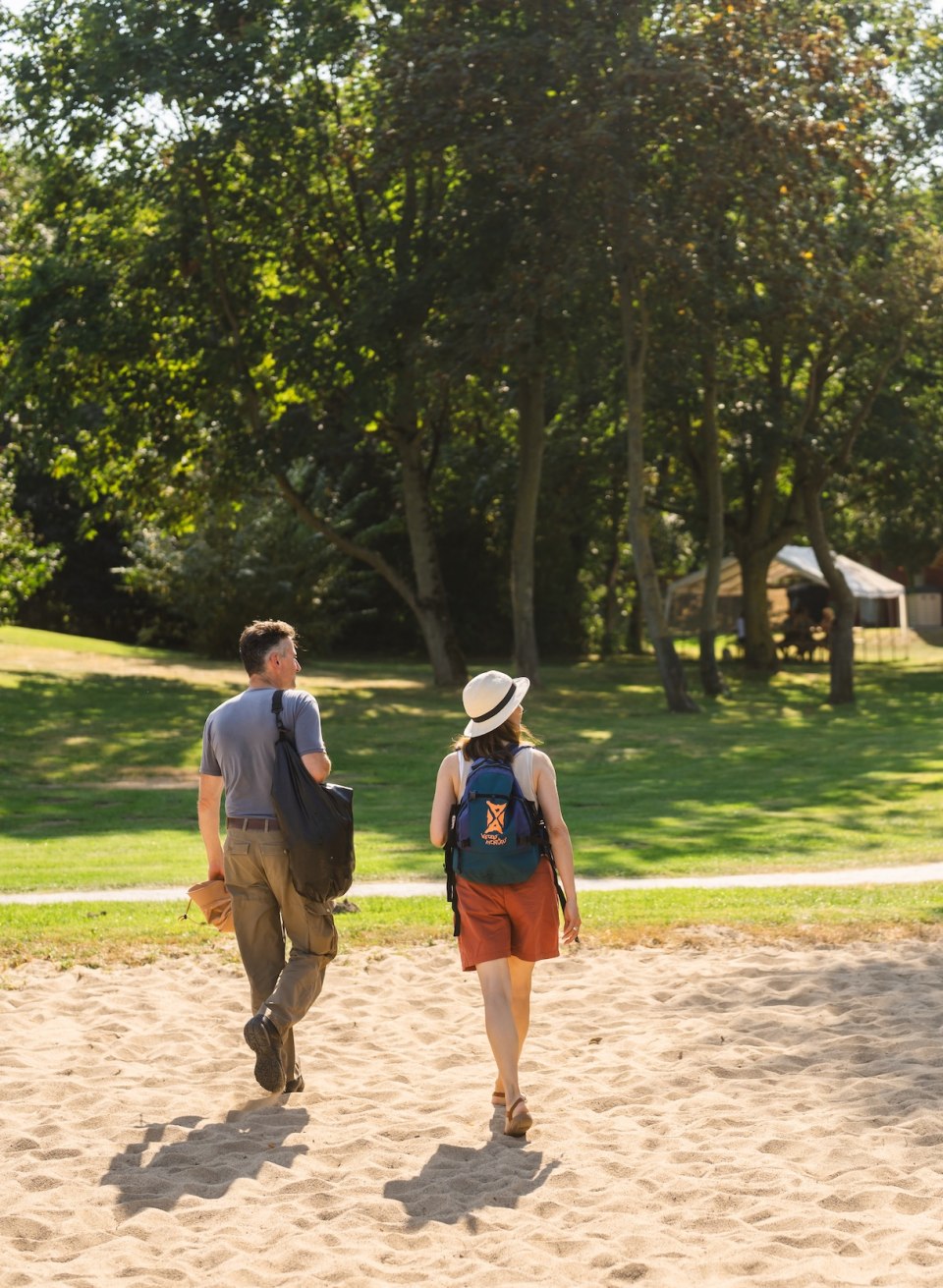 Een stel wandelt door een groen park in de richting van de Stolper Fährkrug, met een bord op de voorgrond.