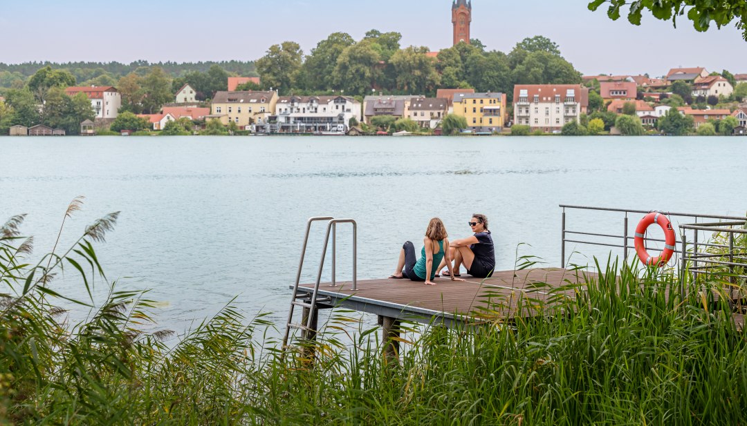 Twee vrouwen zitten op een steiger en kijken uit over een meer // De steiger voor de kliniek biedt een prachtig uitzicht op het meer. // © MV-T/Tiemann Twee vrouwen zitten op een steiger en kijken uit over een meer