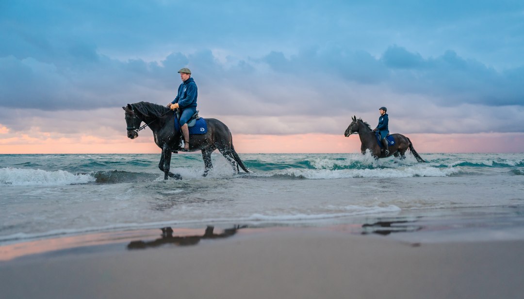 Dwóch jeźdźców na koniach jeździ po plaży o zachodzie słońca nad Morzem Bałtyckim na półwyspie Fischland-Darß-Zingst