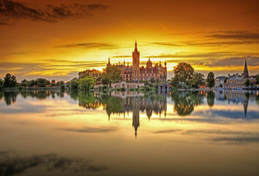 Kasteel Schwerin wordt omlijst door de laatste zonnestralen. De zonsondergang kleurt de lucht oranje. Kasteel Schwerin wordt weerspiegeld in het kalme meer.