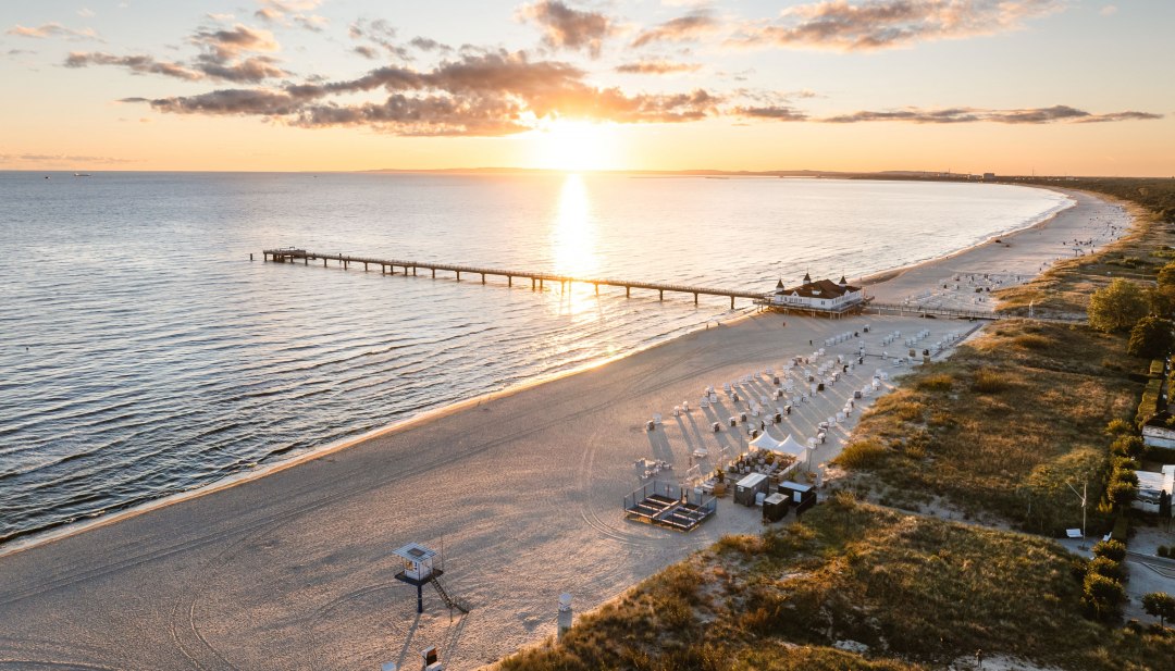 Zdjęcie lotnicze molo w Ahlbeck o wschodzie słońca, plaża i Morze Bałtyckie w złocistym świetle. // Wschód słońca nad Morzem Bałtyckim, molo w Ahlbeck rozciąga się w stronę światła – scena dla ślubnej przysięgi z niesamowitym widokiem. // © MV-T/Gross Zdjęcie lotnicze molo w Ahlbeck o wschodzie słońca, plaża i Morze Bałtyckie w złocistym świetle.