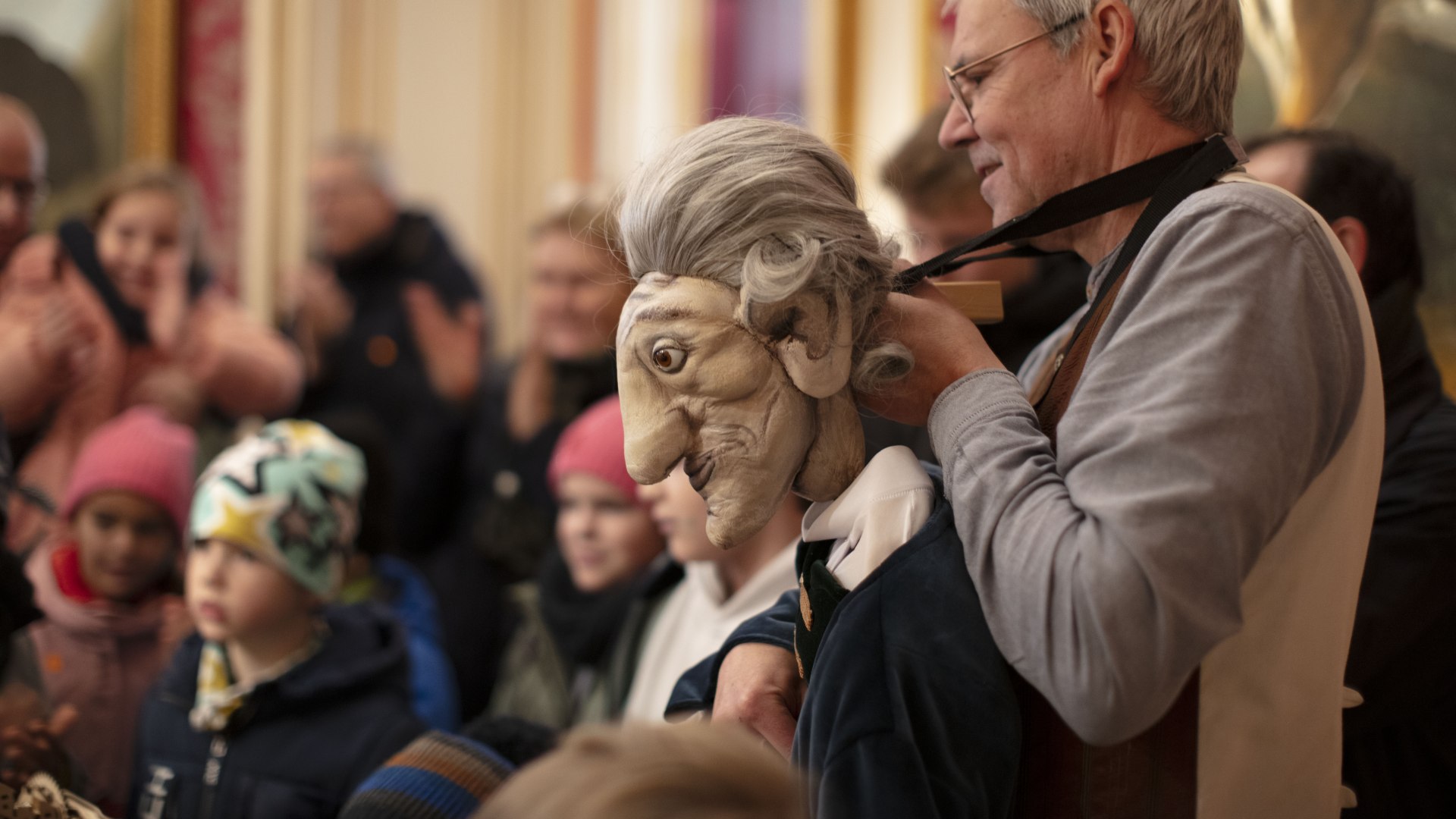 A puppeteer with a large puppet as valet plays in front of an audience.