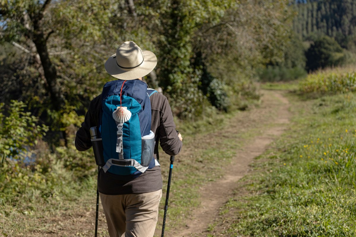Gezicht van achteren op een pelgrim die over een landelijke weg naar Santiago de Compostela loopt. Camino de Santiago, Camino de Santiago // &copy; AdobeStock