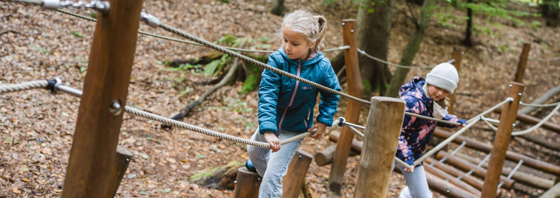 Twee kinderen balanceren op een speelstation in het Kinderheilwald Heringsdorf door het herfstige beukenbos op Usedom.