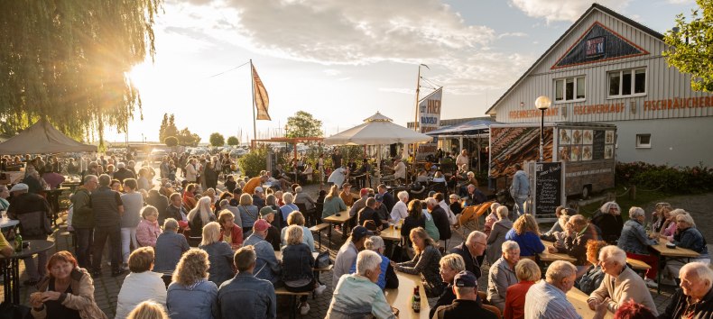 Live-Musik am Ribnitzer Fischhafen: volle Bänke, Gespräche, Fischduft aus der Räucherei – Hafenflair bis in den Abend. // © Ribnitzer Fischhafen / Hugo Scholz-Witzel Live-Musik am Ribnitzer Fischhafen: volle Bänke, Gespräche, Fischduft aus der Räucherei – Hafenflair bis in den Abend. // © Ribnitzer Fischhafen / Hugo Scholz-Witzel