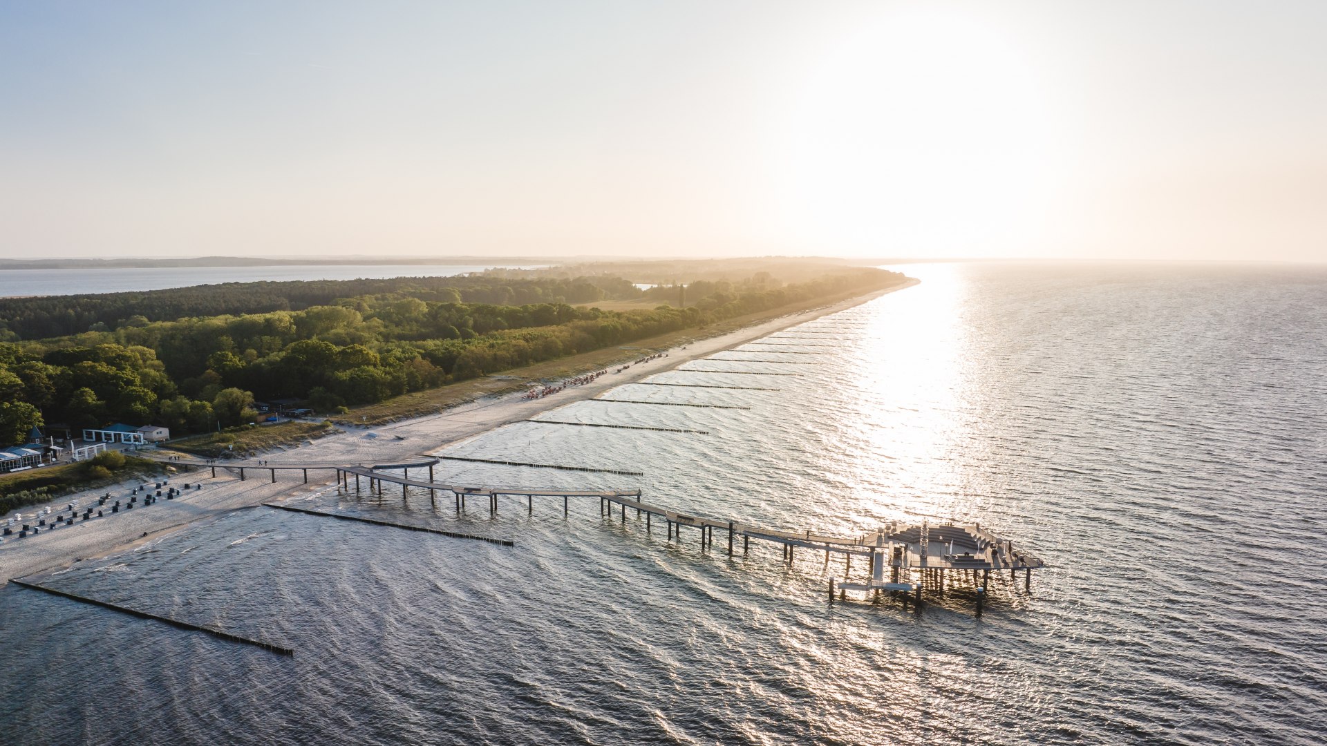 Luchtfoto van de Koserow-pier op Usedom in het warme licht van zonsondergang met het strand en het kustbos op de achtergrond.