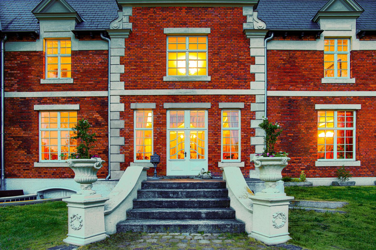 The illuminated entrance to the Brookhusen Manor House: a historicist brick facade and invitingly glowing windows at dusk. // © Herrenhaus Brockhusen The illuminated entrance to the Brookhusen Manor House: a historicist brick facade and invitingly glowing windows at dusk. // © Herrenhaus Brockhusen