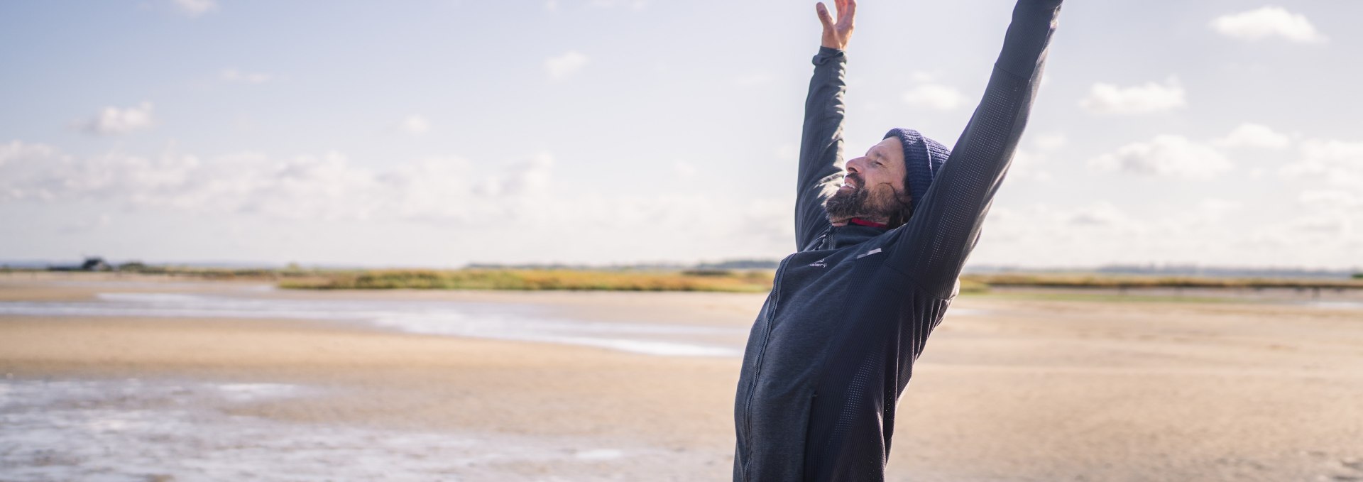 Een man staat met uitgestrekte armen op het strand van Gollwitz op het eiland Poel, onder een strakblauwe hemel.