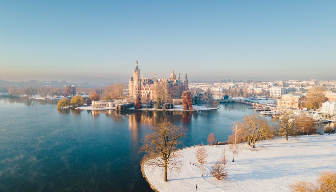 Zamek Schwerin w zimowej warstwie śniegu nad Jeziorem Schwerińskim // Zamek Schwerin z lotu ptaka w zimowej szacie. // © MV-T/Scholz-Witzel Zamek Schwerin w zimowej warstwie śniegu nad Jeziorem Schwerińskim