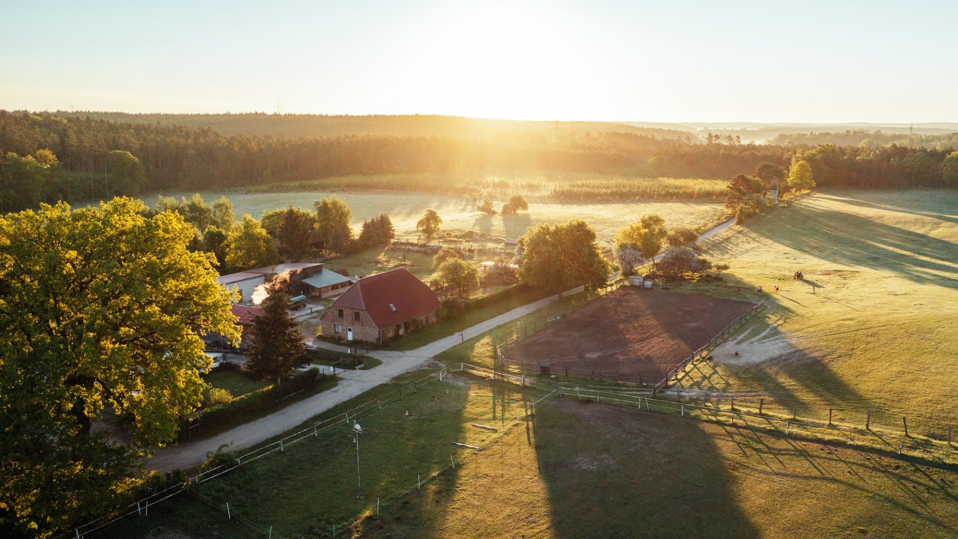 Waldhof Bruchmühle z lotu ptaka o zachodzie słońca. Gospodarstwo z budynkami gospodarczymi i wybiegiem // Tylko natura: Waldhof Bruchmühle leży między łąkami, lasami i jeziorami. // © MV-T/Gänsicke Waldhof Bruchmühle z lotu ptaka o zachodzie słońca. Gospodarstwo z budynkami gospodarczymi i wybiegiem