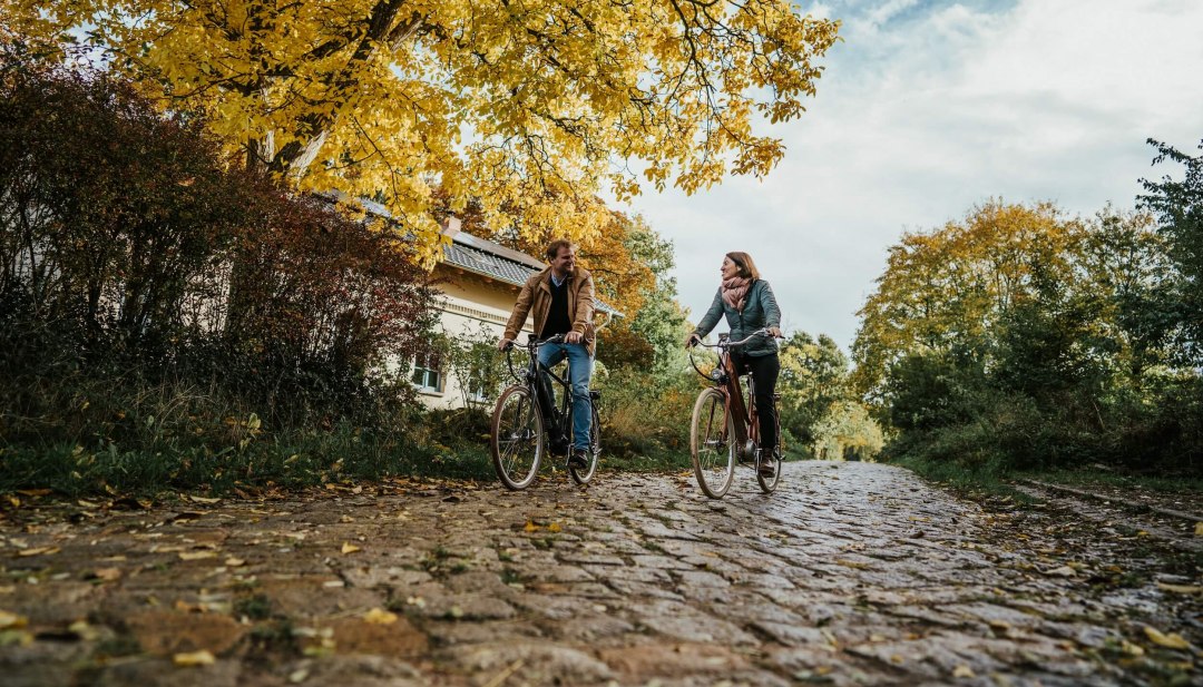 Twee mensen fietsen op kasseien in de buurt van het landgoed Pohnstorf in de herfst. // Op stap met de fiets op het landgoed Pohnstorf in de herfst // © 1000seen Twee mensen fietsen op kasseien in de buurt van het landgoed Pohnstorf in de herfst.