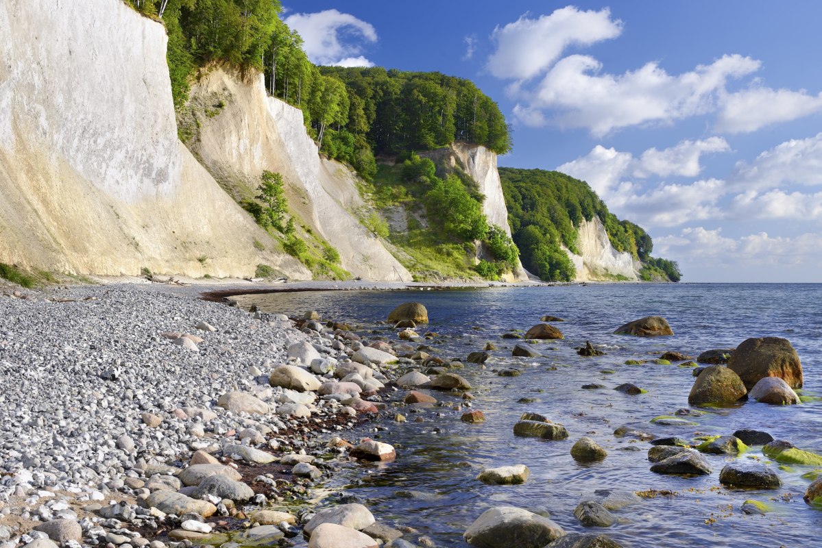 Ronde stenen omzomen het strand, zachte golven spoelen rond met mos bedekte rotsblokken. De witte krijtrotsen van het Nationaal Park Jasmund torenen majestueus uit boven de Oostzee, bekroond door weelderig beukengroen. Een plek waar je de stilte kunt horen en de kracht van de natuur kunt voelen. // © Francesco Carovillano Ronde stenen omzomen het strand, zachte golven spoelen rond met mos bedekte rotsblokken. De witte krijtrotsen van het Nationaal Park Jasmund torenen majestueus uit boven de Oostzee, bekroond door weelderig beukengroen. Een plek waar je de stilte kunt horen en de kracht van de natuur kunt voelen. // © Francesco Carovillano