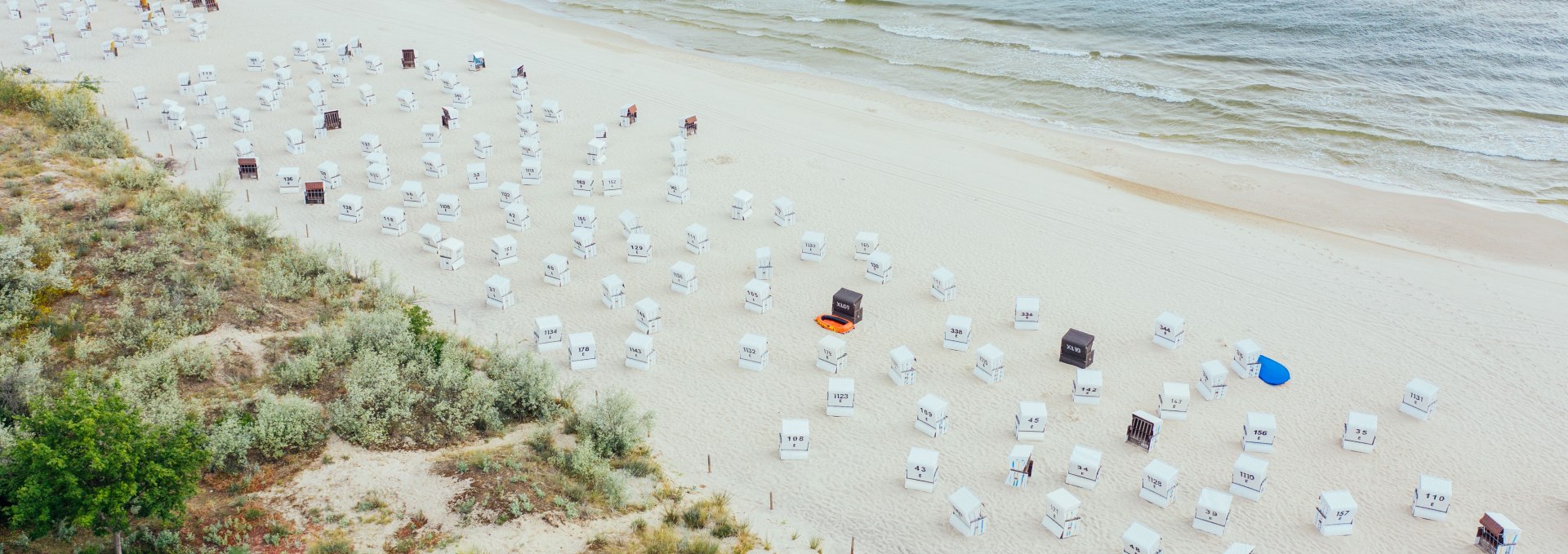 Luchtfoto van het strand in Heringsdorf met talrijke witte strandstoelen en de kalme Baltische Zee op de achtergrond.