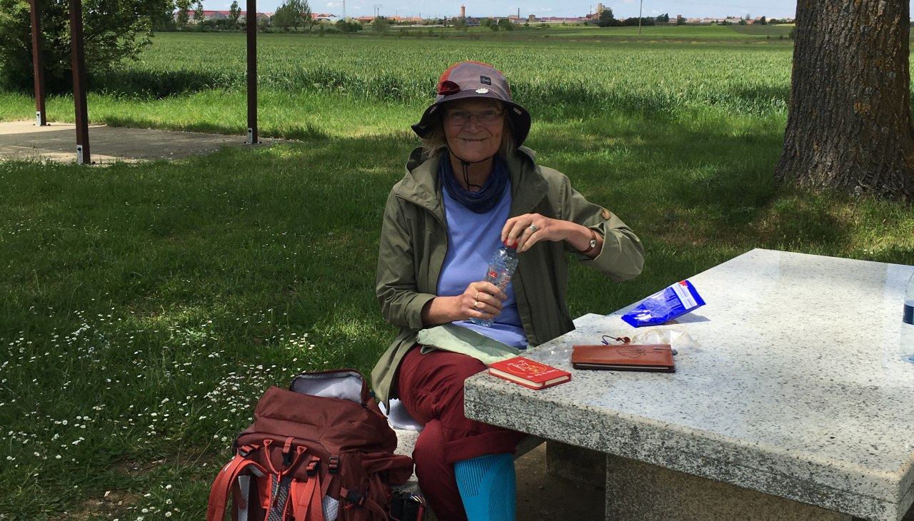 Pani Wahmkow siedzi przed łąką i piknikuje przy kamiennym stole., © Christine Wahmkow