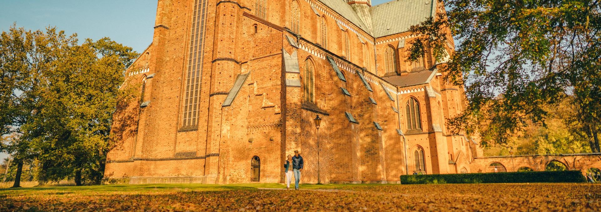 Para spaceruje przed Bad Doberan Minster jesienią. Liście leżą na ziemi przed katedrą.