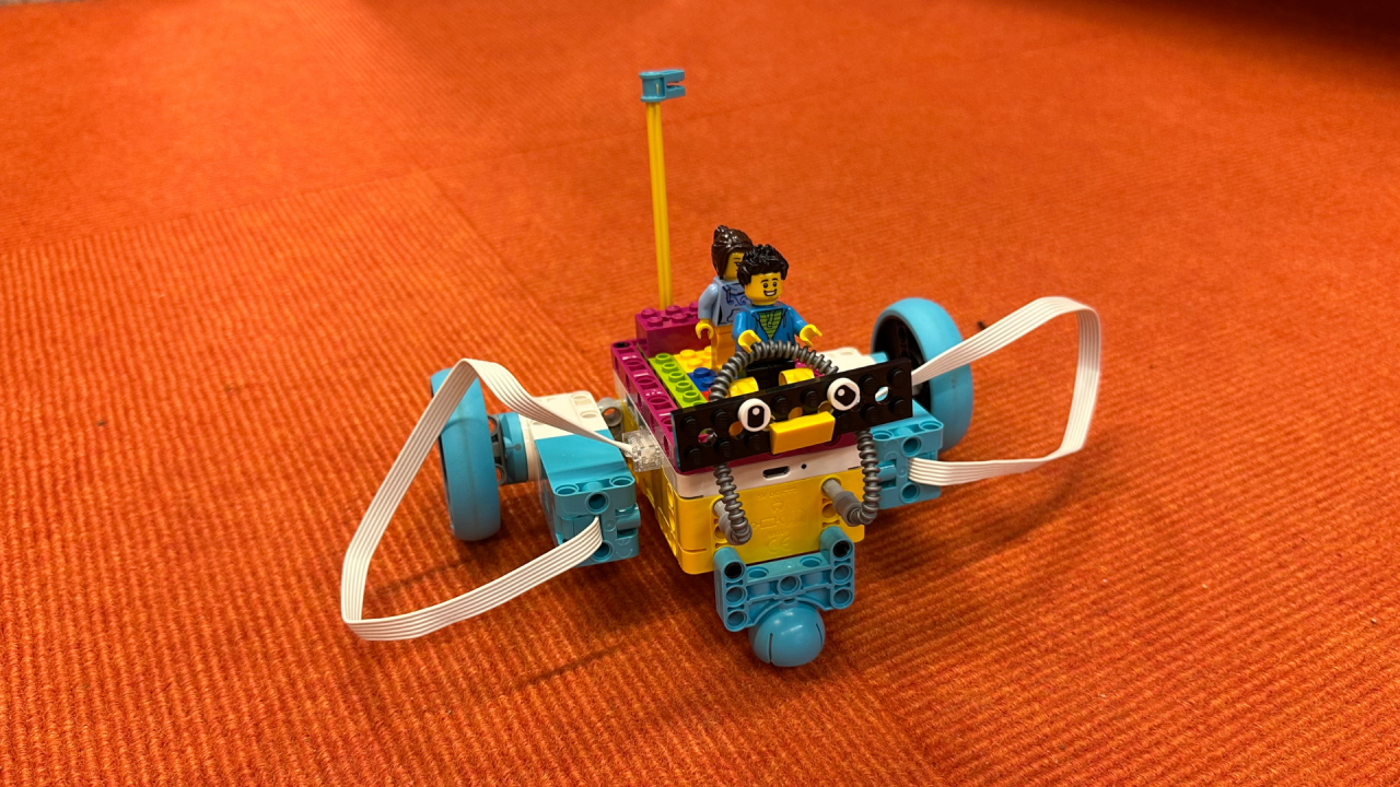 mały robot Lego z dwiema figurkami Lego na pomarańczowym tle // &copy; Stadtbibliothek Stralsund