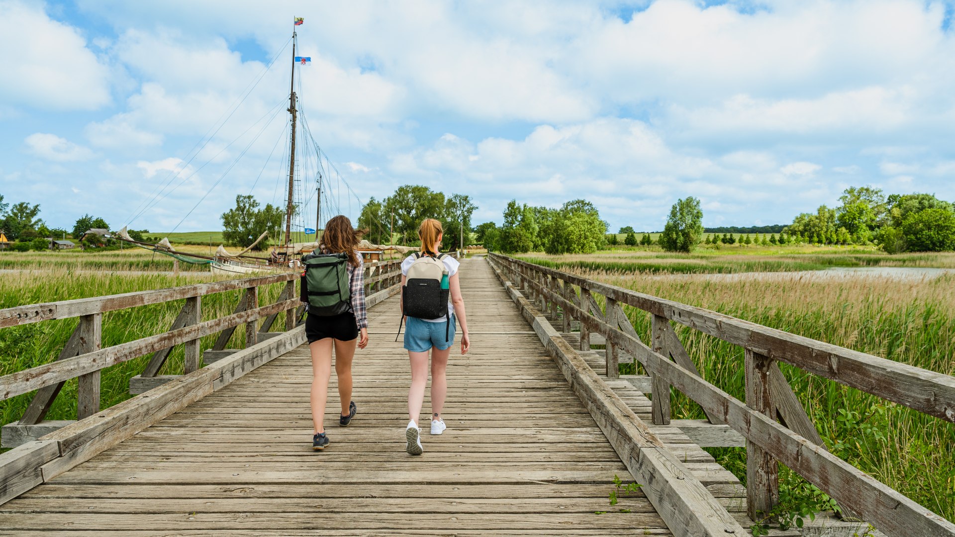 Two women walk across the Lebbin wooden bridge on the island of Rügen // On the creaking wooden planks of the Lebbin bridge, the hiking trail leads across the Liddow stream, past the Liddow museum harbor. // © MV-T/Tiemann Two women walk across the Lebbin wooden bridge on the island of Rügen