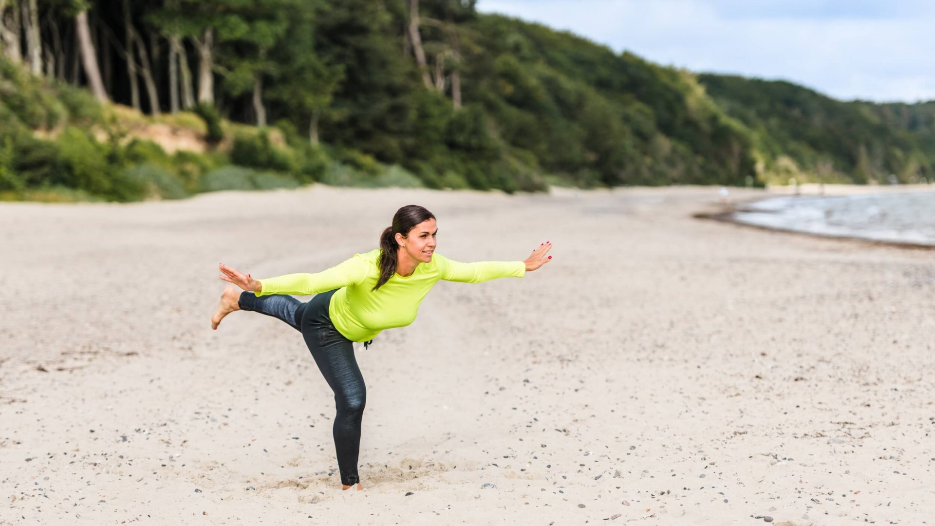 Een vrouw doet de &quot;staande balans&quot; op het strand en houdt haar evenwicht.