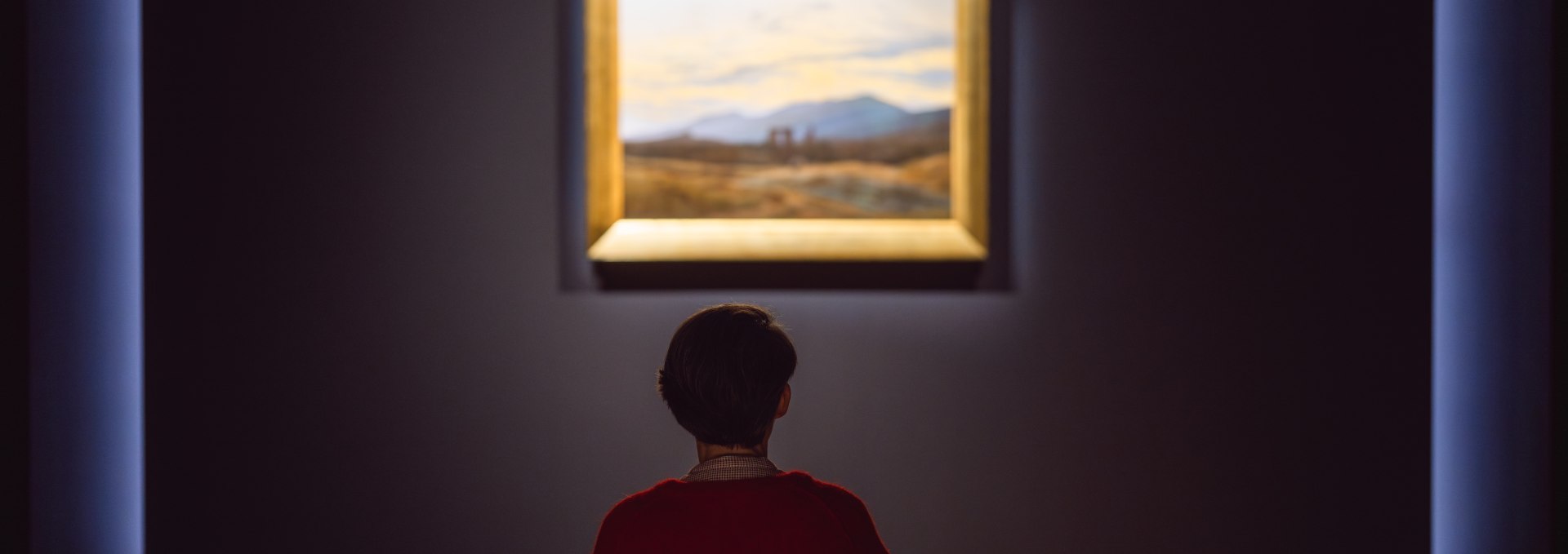 Visitor sits in front of a romantic landscape painting in the gallery of the Pomeranian State Museum.