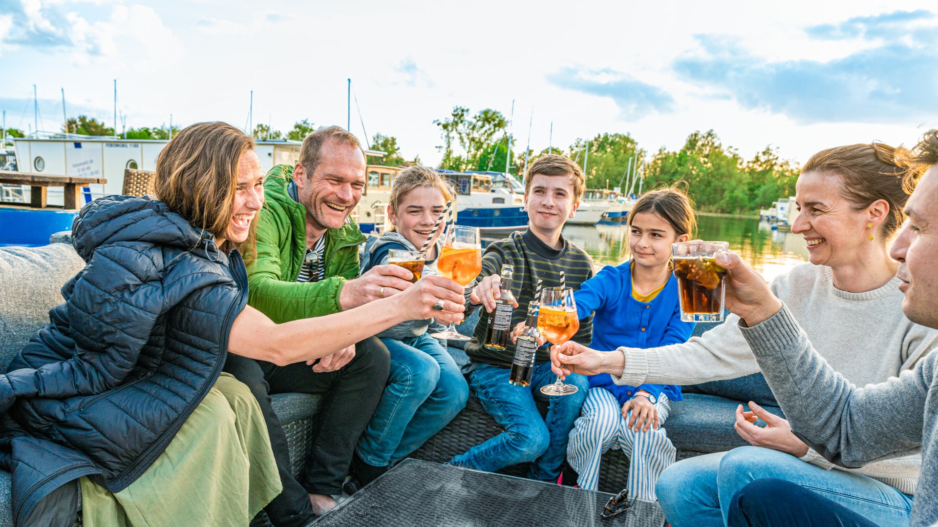 Two families clink glasses in the Pirate's Bar. // A nice end to the day at Pirate's Bar: the two friendly families toast to a great vacation with their feet in the sand. // © MV-T/Tiemann Two families clink glasses in the Pirate's Bar.