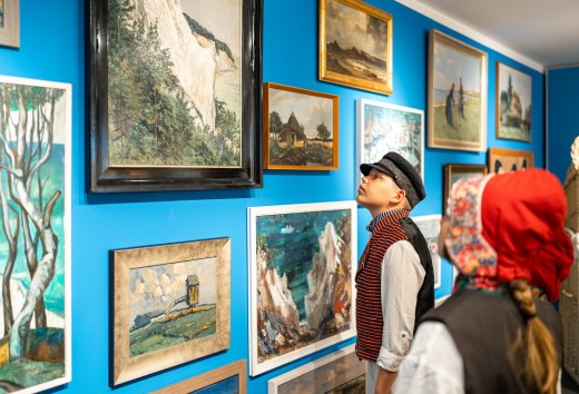 In het streekmuseum van Mönchgut hangen tekeningen en schilderijen aan de muur - kinderen staan er in traditionele kleding voor en bestuderen ze.