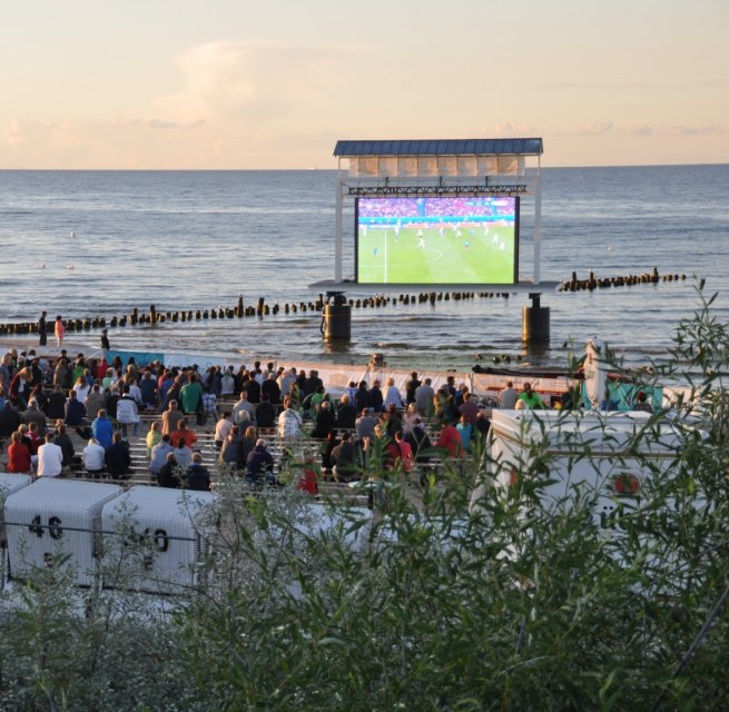 Eine große Menge schaut am Strand auf eine Leinwand im Wasser, dahinter liegt das ruhige Meer. // Fußball läuft auf der Großleinwand, das Publikum sitzt am Meer und teilt den Moment bis javascript://in den Abend. // © Eigenbetrieb Kaiserbäder Insel Usedom Eine große Menge schaut am Strand auf eine Leinwand im Wasser, dahinter liegt das ruhige Meer. // Fußball läuft auf der Großleinwand, das Publikum sitzt am Meer und teilt den Moment bis javascript://in den Abend. // © Eigenbetrieb Kaiserbäder Insel Usedom