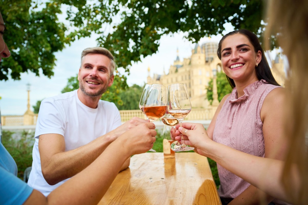 Guests raise a glass of wine at the Schwerin Wine Festival in the Alter Garten. In the background, Schwerin Castle rises up, providing a unique backdrop for the festival. // &copy; LHSN/Celien Graubaum