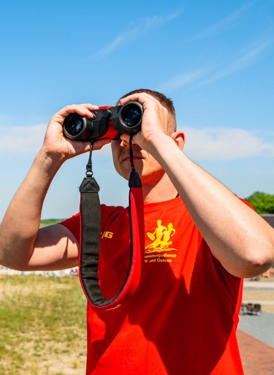 A lifeguard looks out over the beach in Graal-M&uuml;ritz with binoculars and observes the Baltic Sea in clear summer weather.