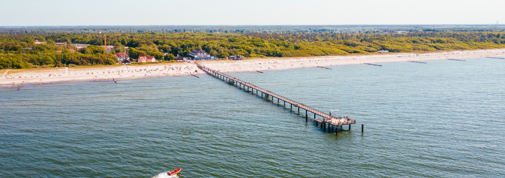 Luchtfoto van de pier in het kuuroord Graal-Müritz aan de Baltische Zee, die ver uitsteekt in de Baltische Zee, omgeven door een zandstrand en dichte groene bossen op de achtergrond.